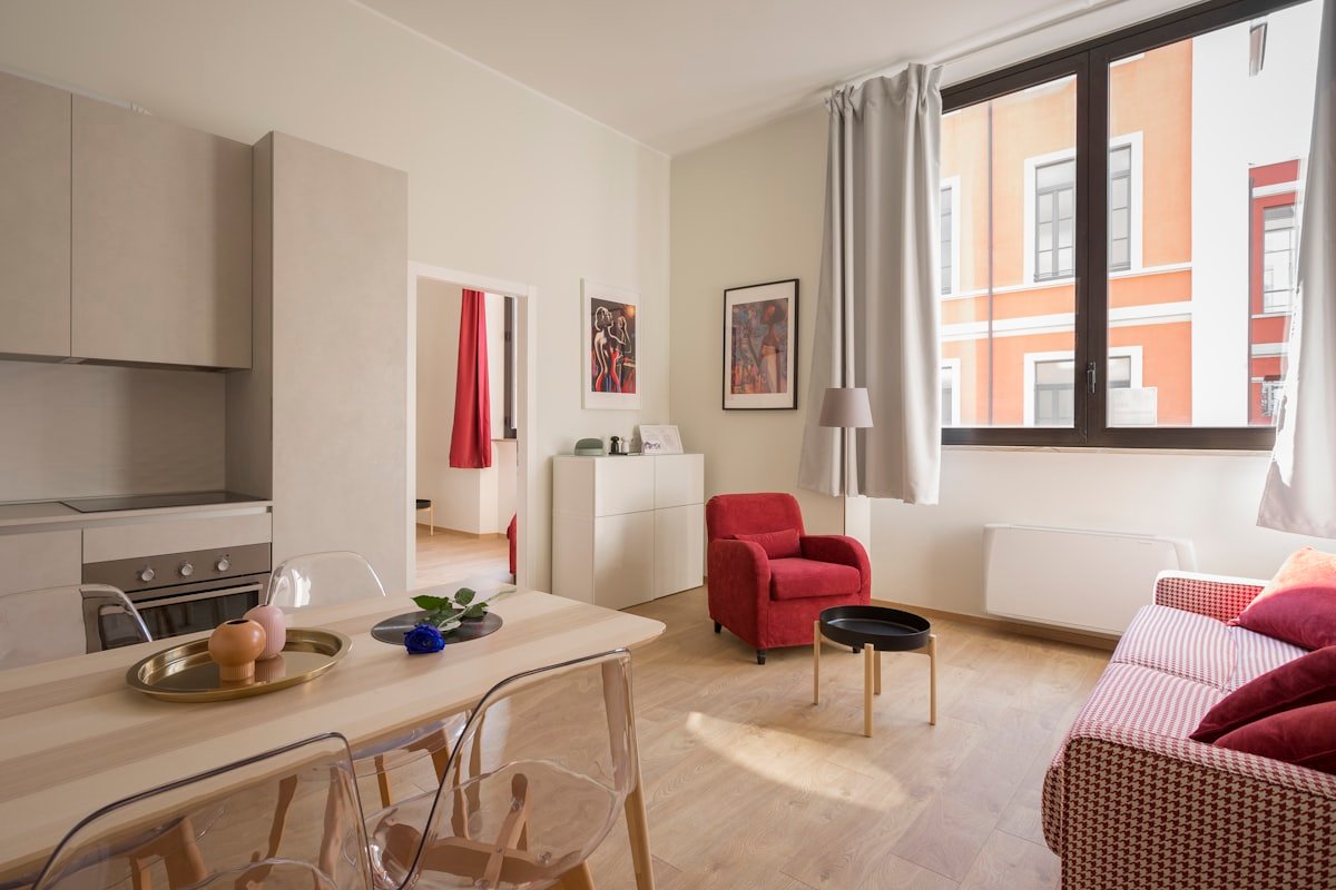 Apartamento con cocina abierta, mesa de comedor de madera clara y sillón rojo